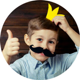 Boy giving a thumbs up and wearing a fake moustache and holding a fake gold crown above his head.