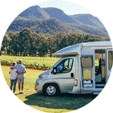 A couple standing next to an RV park on green grass looking at a mountain range.