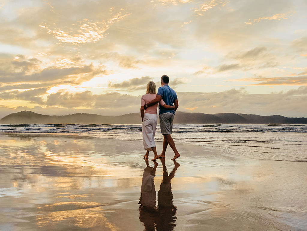 Couple walking along the water's edge of a beach at sunset.