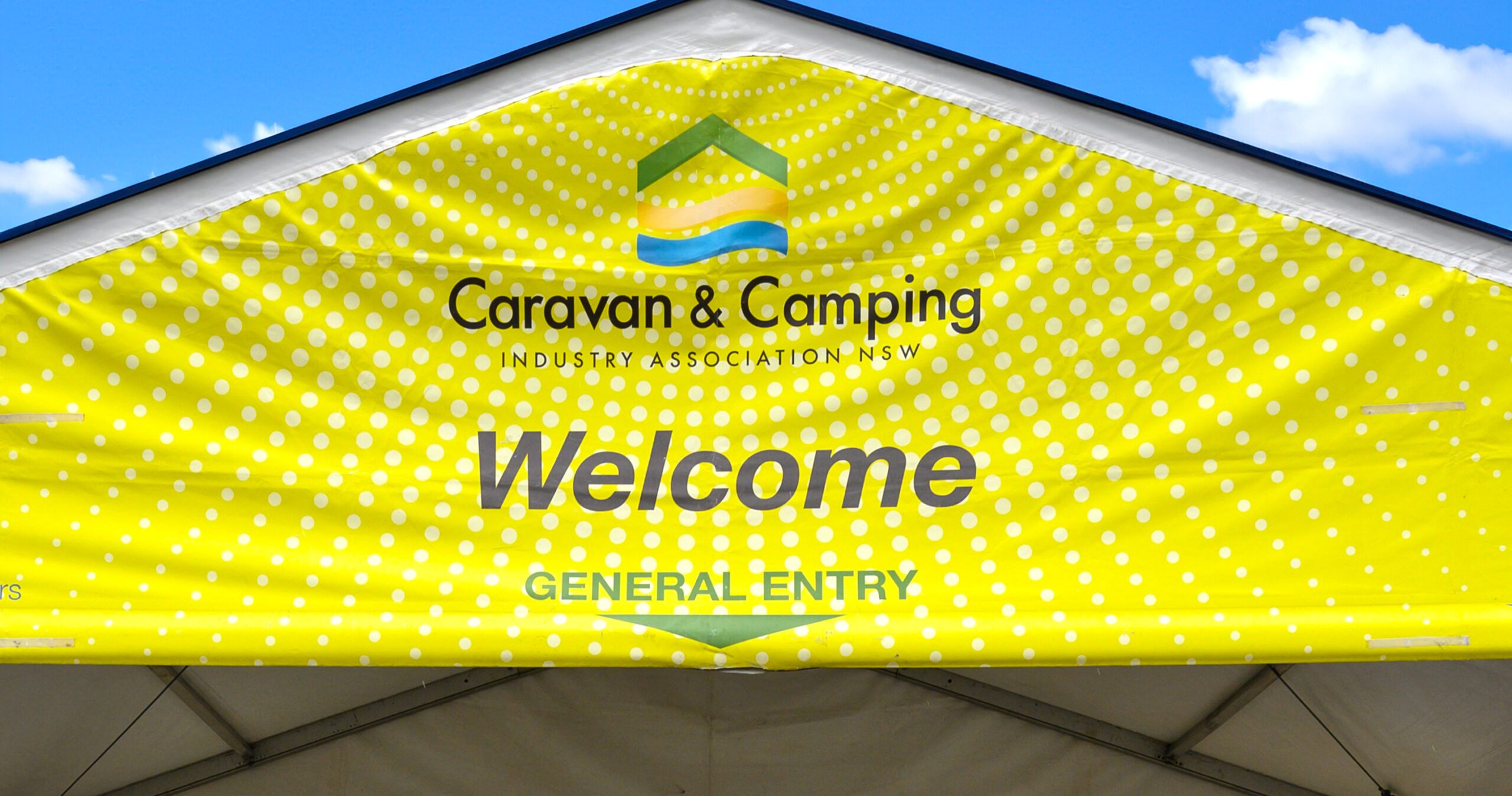 Caravan and Camping Expo welcome sign on an yellow/green arch way entrance with blue skies.