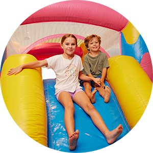 a young boy and girl sitting on a slide of a jumping castle.
